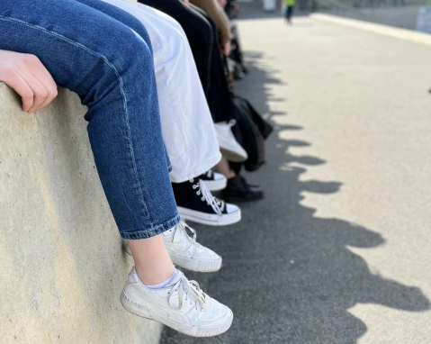 Auf einer Mauer sitzen junge Menschen, man sieht jeweils nur die Beine vom Knie abwärts