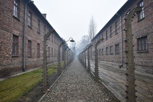 Zwischen Gebäuden verläuft ein Weg zwischen Stacheldrahtzäunen